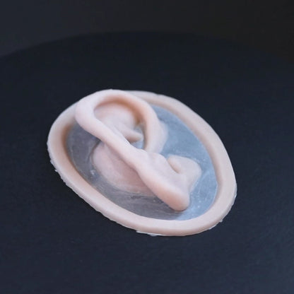 Silicone Ear prosthetic in vanilla shade on a black turntable, slowly rotating. 