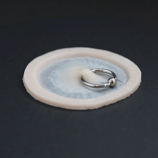 Surface piercing, with ring, prosthetic in vanilla shade on a black turntable, slowly rotating. 