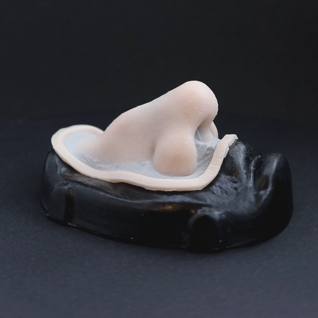 A crooked nose prosthetic in vanilla shade on a black turntable, slowly rotating. 