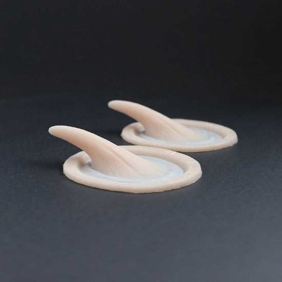 Pair of large vertical horns prosthetics in vanilla shade on a black turntable, slowly rotating. 