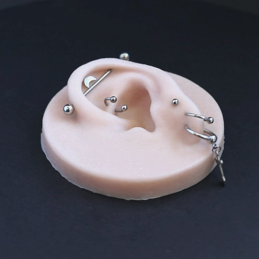 A silicone ear display piece with several earrings and piercings, on a black turntable, slowly rotating. 