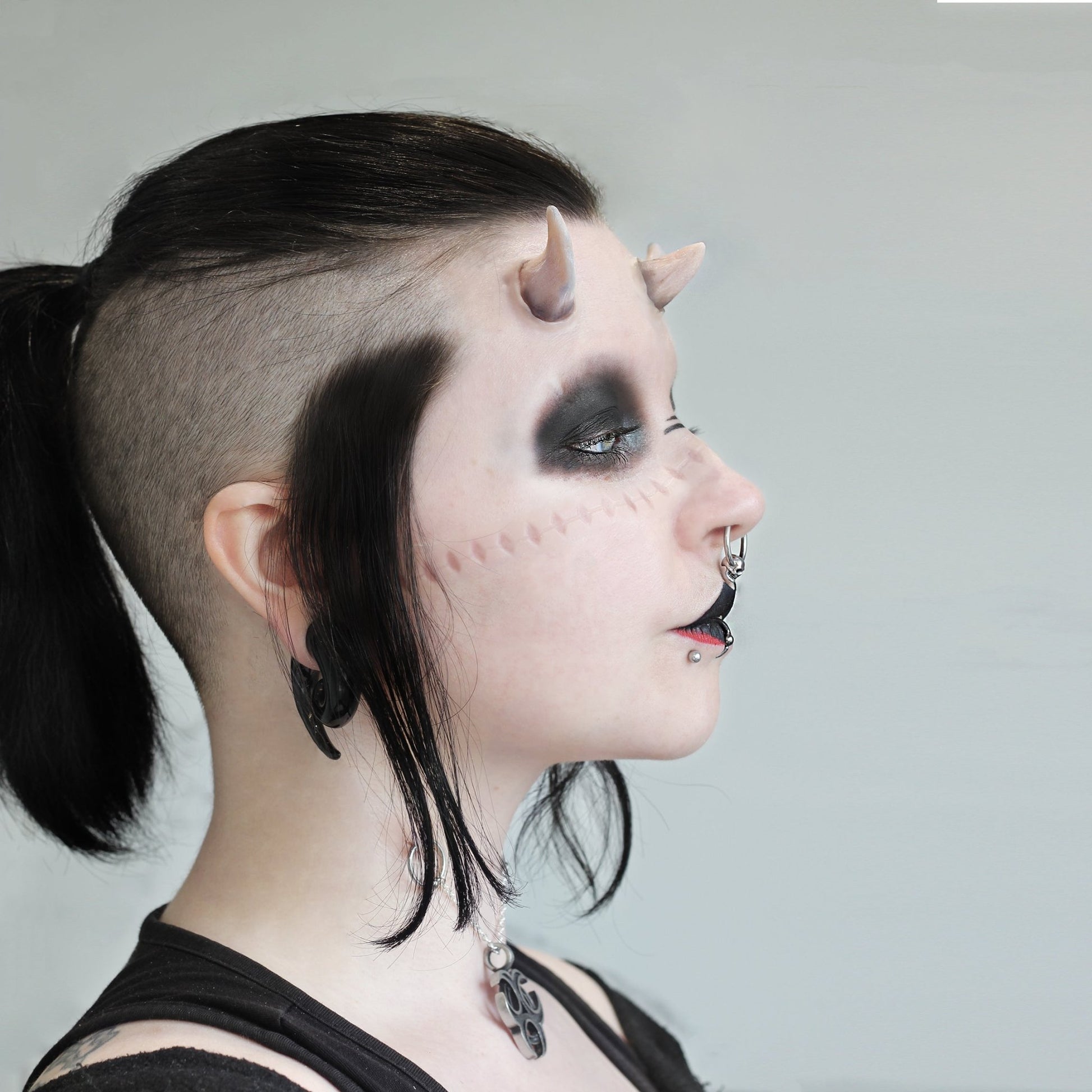 Woman with black hair wearing crooked horns and dark makeup