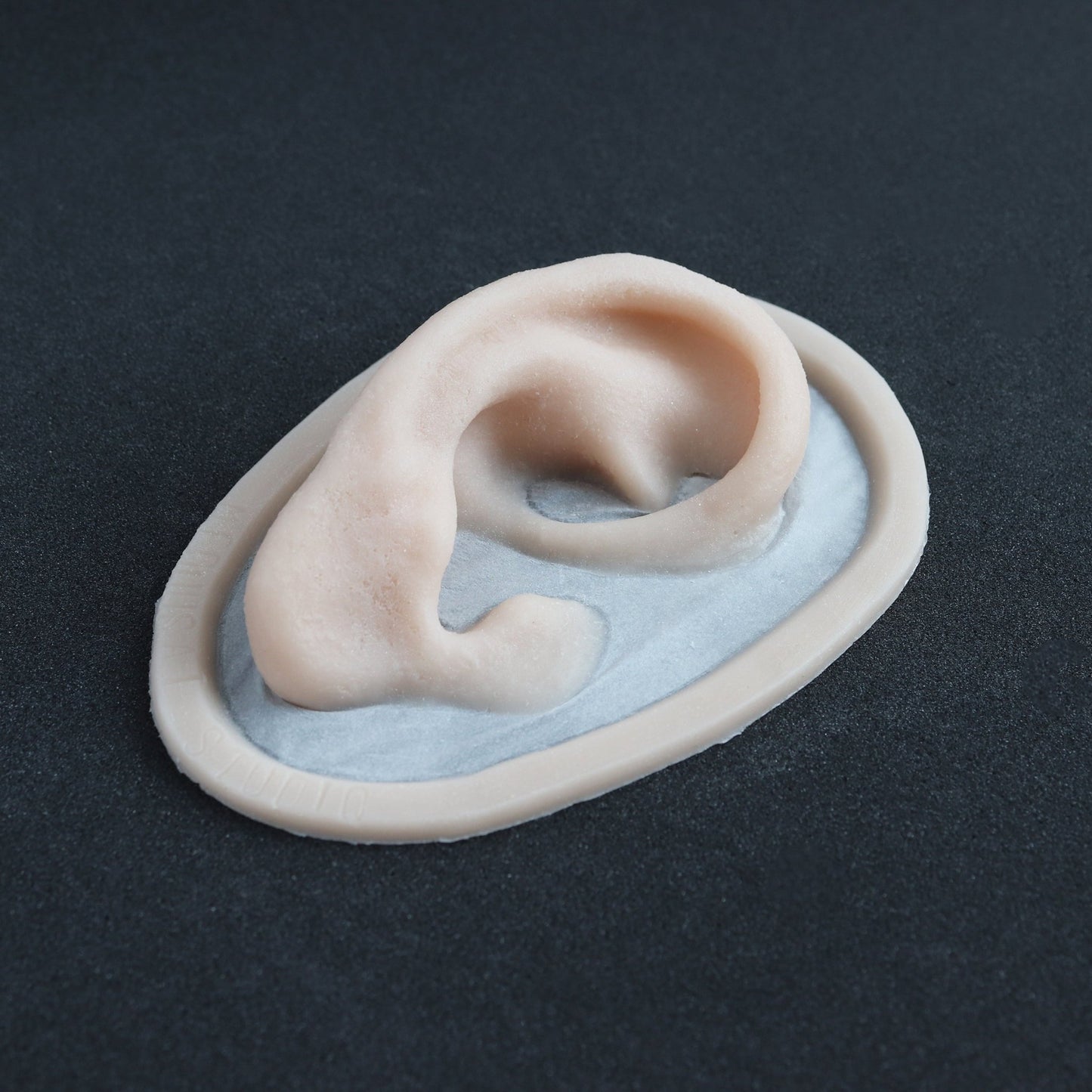 Extra Ears - Silicone makeup prosthetic in vanilla shade on a black surface