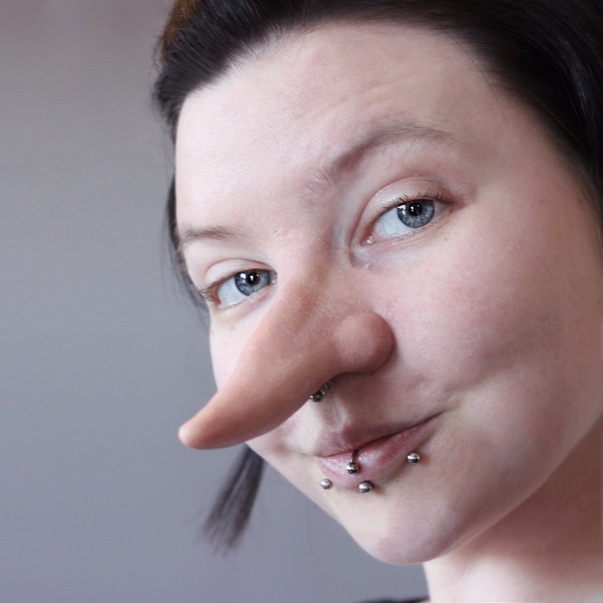 Woman with dark hair wearing a long nose prosthetic
