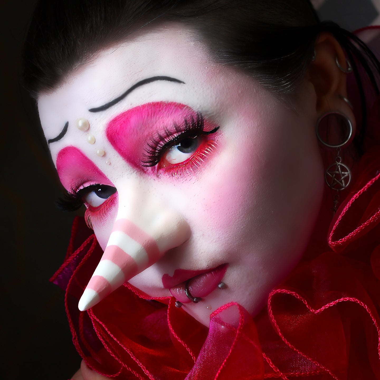 Woman in pink clown makeup, wearing a long nose prosthetic