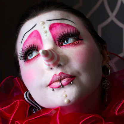 Woman in pink clown makeup, wearing a long nose prosthetic