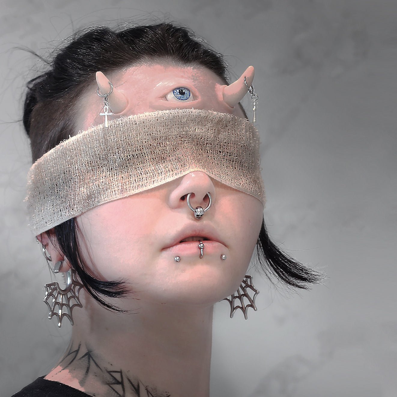 Woman in a blindfold wearing pierced horns and a third eye prosthetic