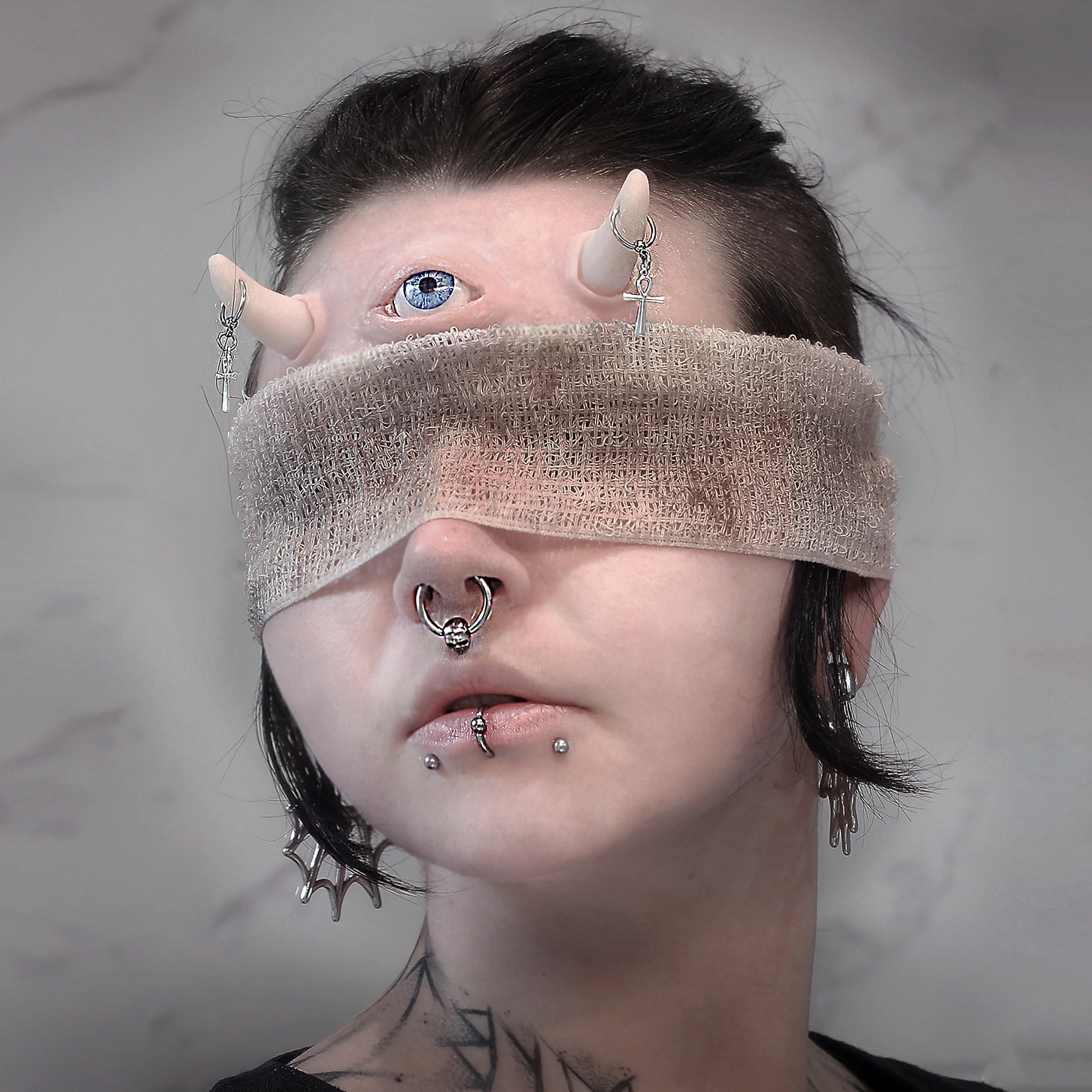 Woman in a blindfold wearing pierced horns and a third eye prosthetic