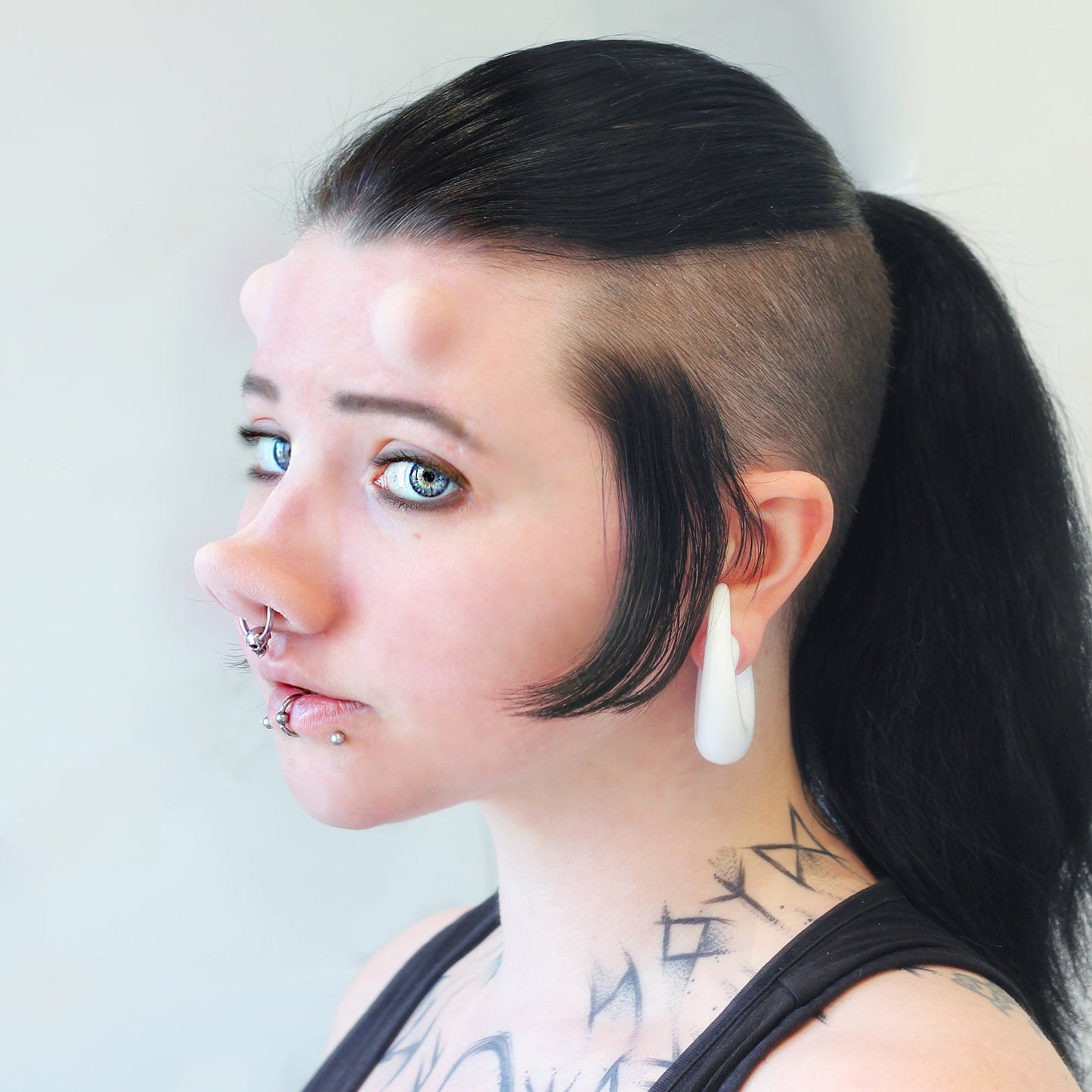 Woman with black hair wearing subdermal horns and a piglet nose prosthetic