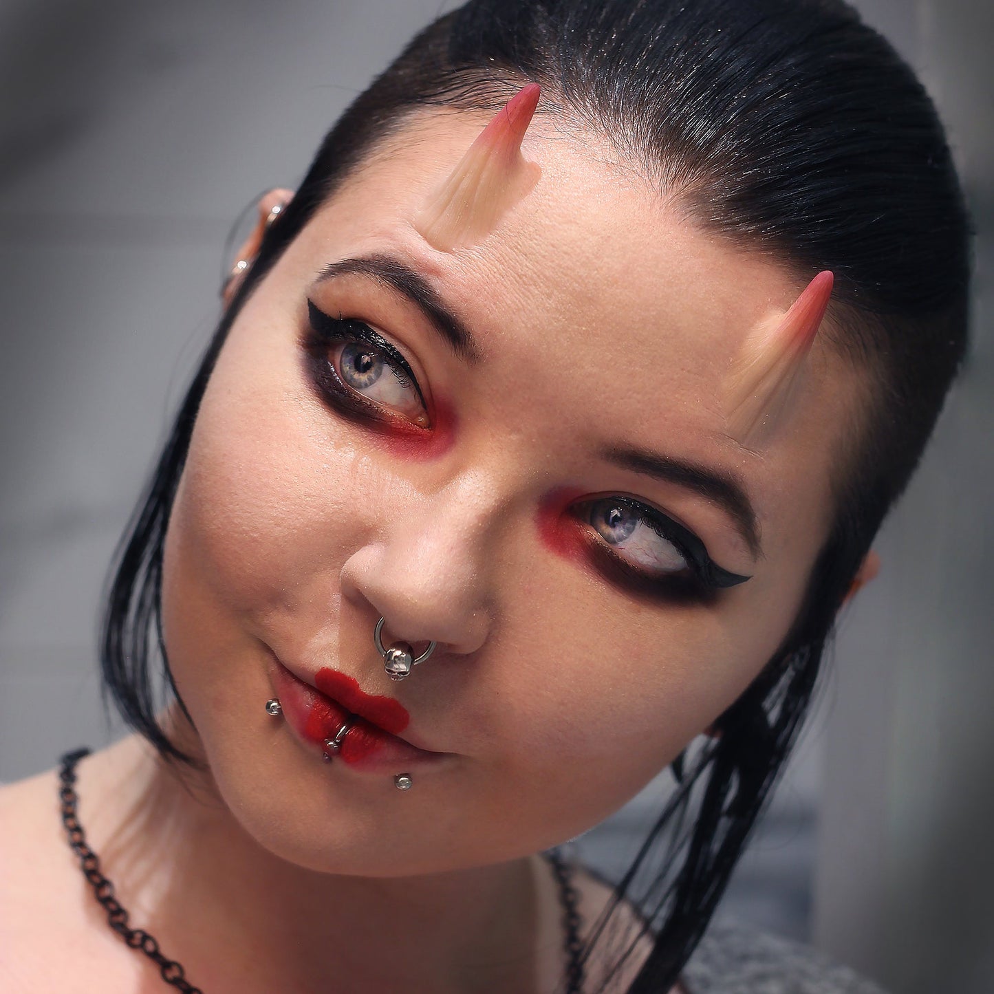 Woman with dark hair wearing red makeup and small vertical horns