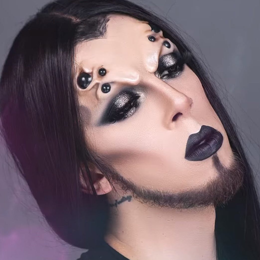Man wearing dark makeup and  spider eyes prosthetics on his forehead