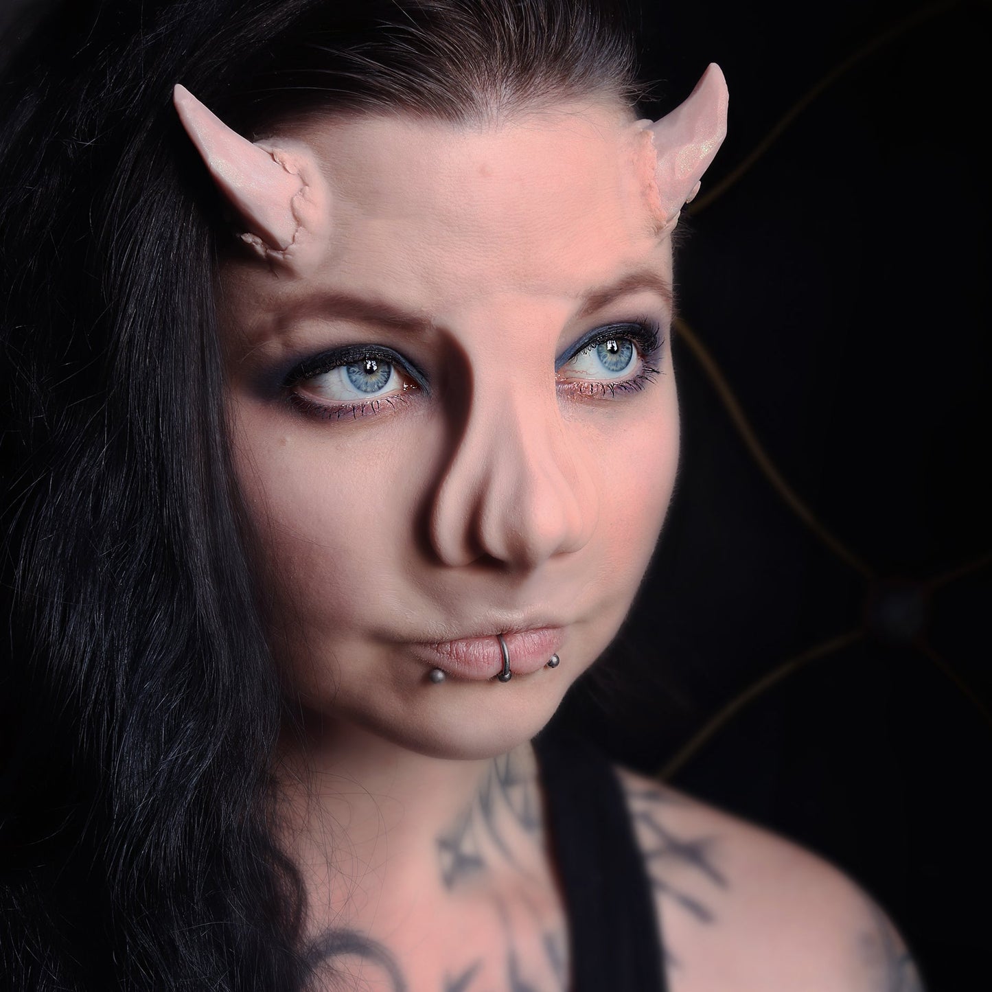 Woman with black hair wearing torn horns and a whelk nose prosthetic